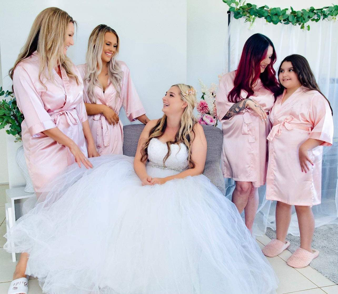 Bridal Party picture with the Bride to Be seated, she is smiling at her 3 Bridesmaids and Flowergirl who are wearing Luxurious Satin Robes in a Rose Gold Colour